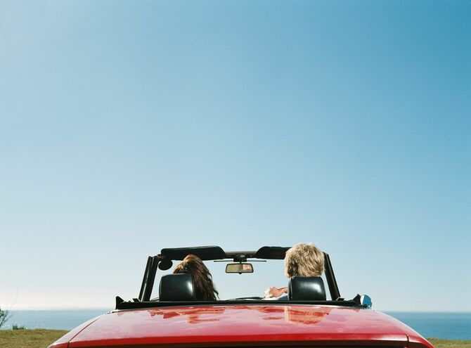 海辺に駐車した赤いスポーツカーに乗るカップル