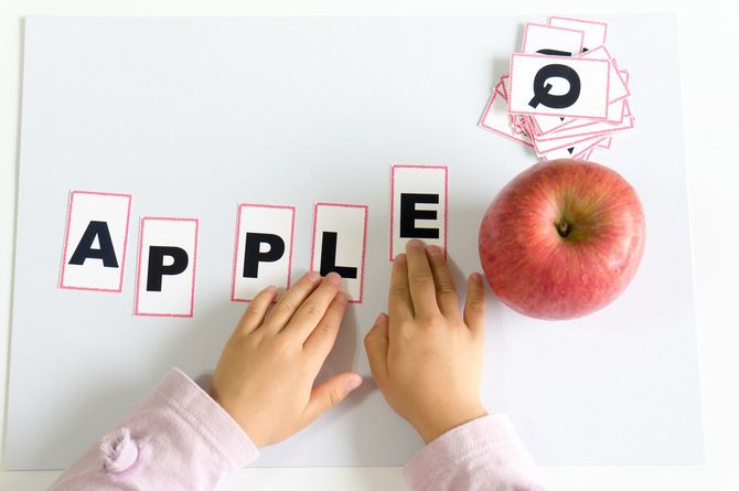 アルファベットのカードを並べて「APPLE」を作る子どもの手