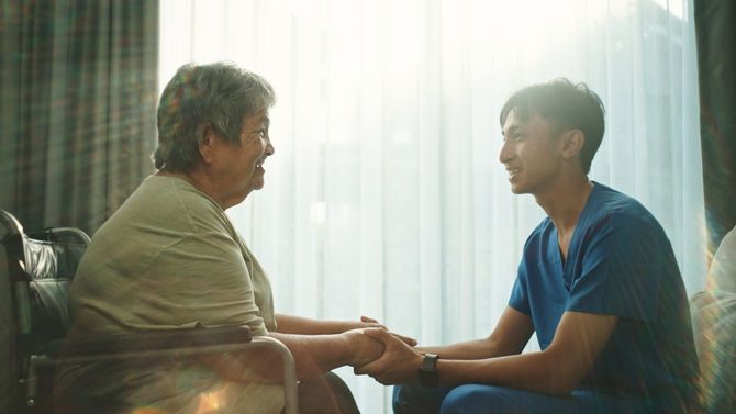 椅子に座った高齢者に笑顔で話す若い医療者