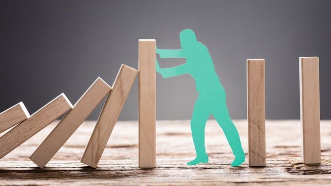 ドミノの連鎖倒壊を防いでいる人のイメージ