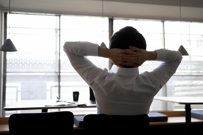 デスクで頭の後ろで腕を組んで一休みしている男性