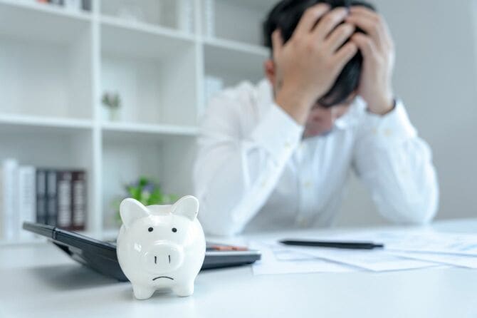 豚の貯金箱と電卓、頭を抱える男性