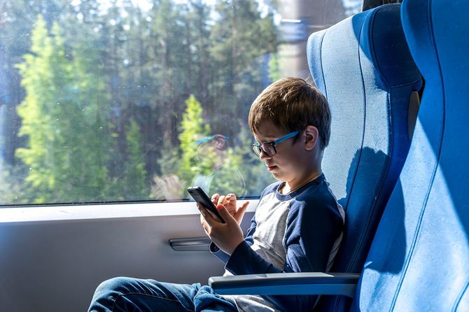 電車の中でスマホを使用する眼鏡をかけた子ども