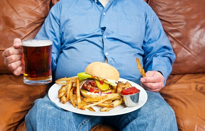 太りすぎの男性が膝の上に非常に大きな不健康な食事