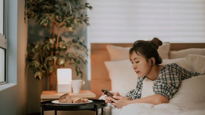 朝、ベッドの上でスマホで音声サービスを楽しむ女性