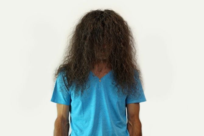 伸びた巻き毛の前髪が顔を覆っている男性