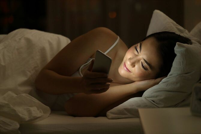 夜、ベッドでスマホを使用する女性