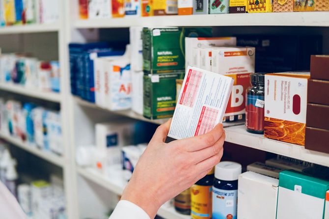 薬局の棚に薬を並べる薬剤師の手元