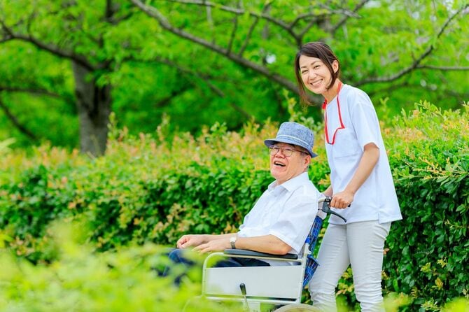公園を散歩する介護士と車椅子の男性