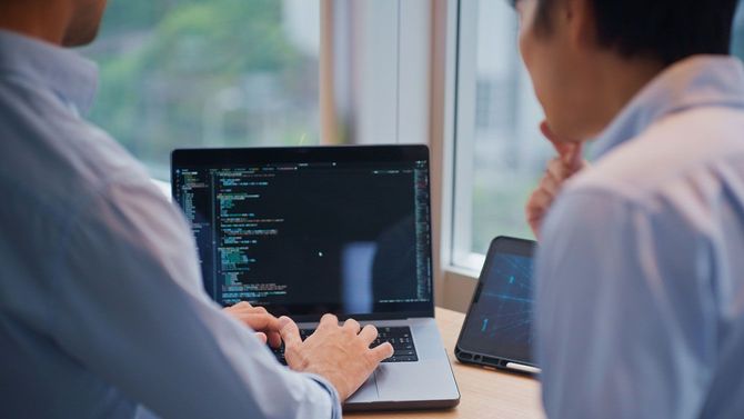 パソコンでソースコードを確認する2人のITエンジニア