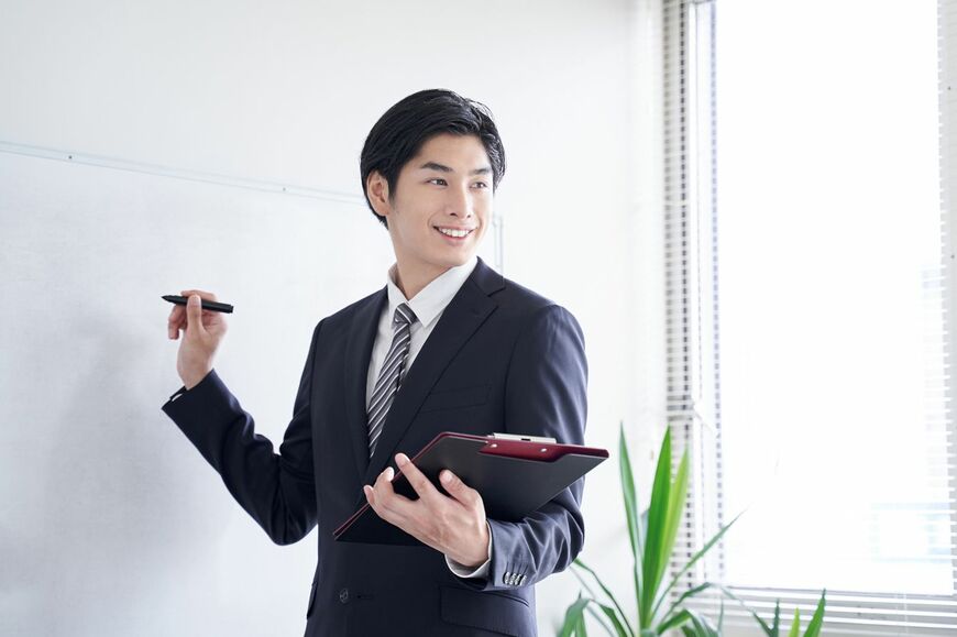 ホワイトボードの前に立ち、自信ありげな表情を見せる男性