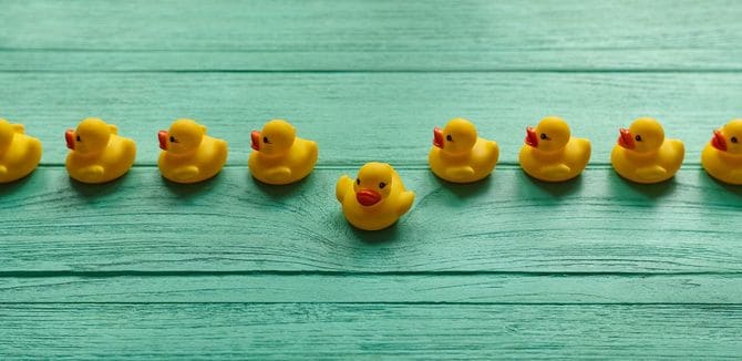 並んだ列から一つだけはみ出たアヒルのおもちゃ