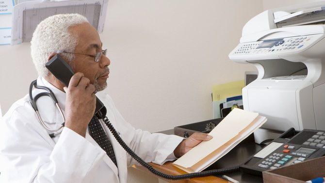 アフリカ系アメリカ人の老人男性医師が記録を確認しながら電話している