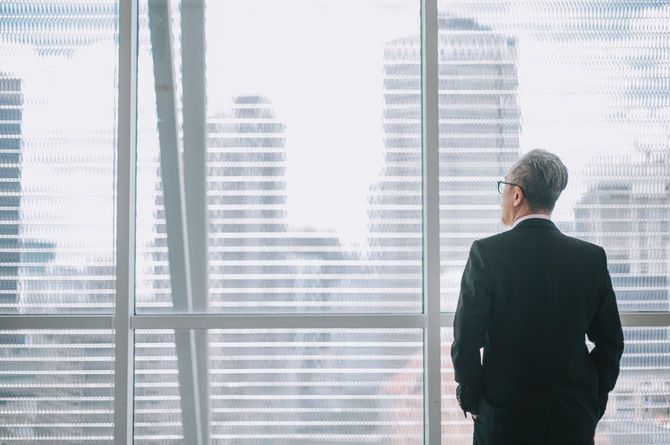 オフィスでポケットに手を入れ外を見ている老齢のビジネスマン
