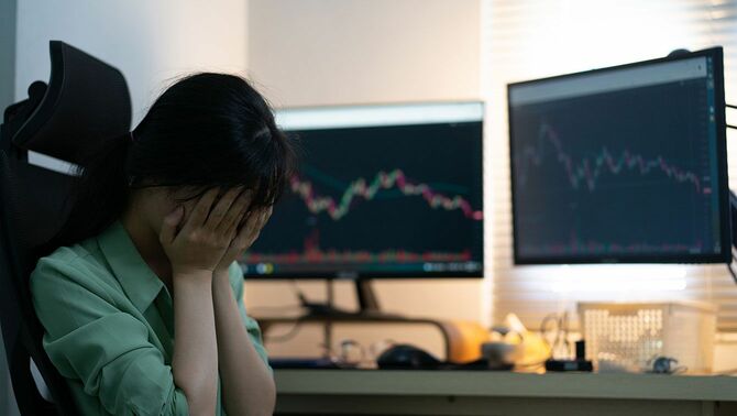 コンピューター上で株取引をしながら手で顔を覆う女性