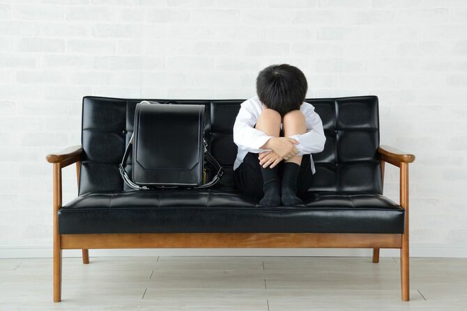ソファーの上にランドセルを置き、その横でひざを抱えて泣いている男の子