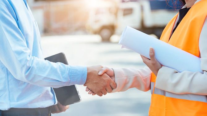 ノートパソコンを持つ土木技師と女性作業員が握手