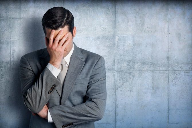 壁にもたれ頭を抱えるビジネスマン