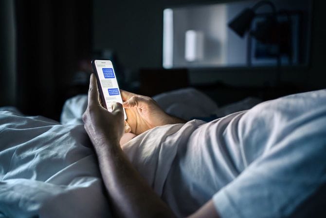ベッドに入り、スマホでテキストメッセージを送っている人