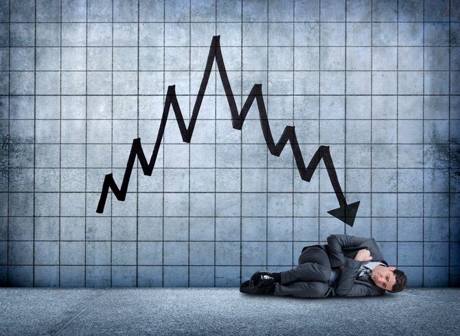 株価の下落チャートの前でうずくまる男性