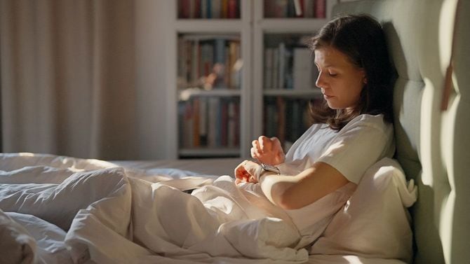 朝、ベッドでスマートウォッチを見ている女性