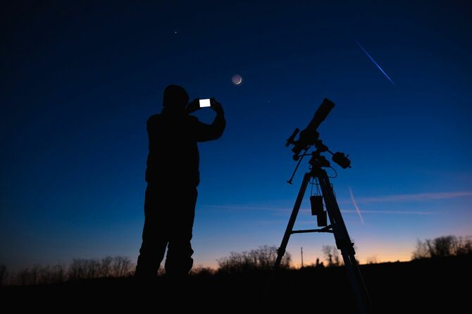望遠鏡の隣で、スマホで天体を撮影しようとしてる男性