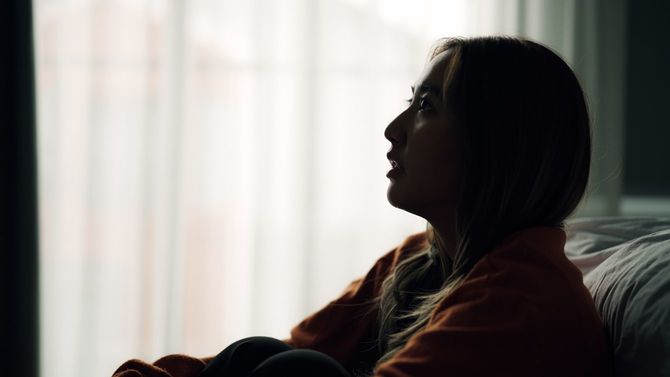 暗い部屋でひざを抱えてベッドに寄りかかっている女性