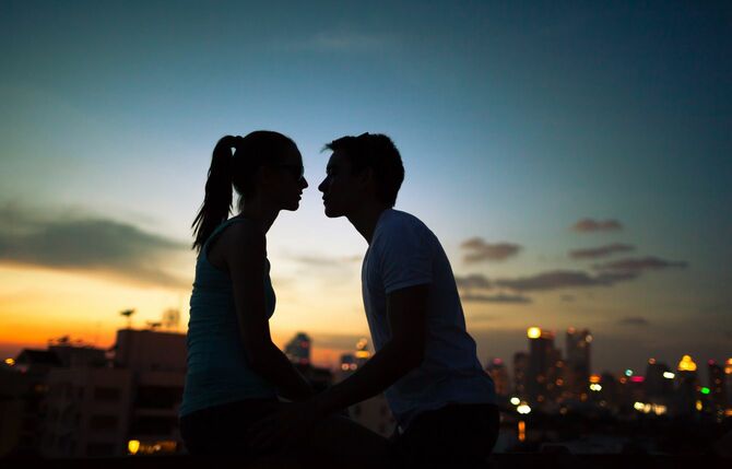 夕焼けに染まる街をバックにキスをしようとしているカップル