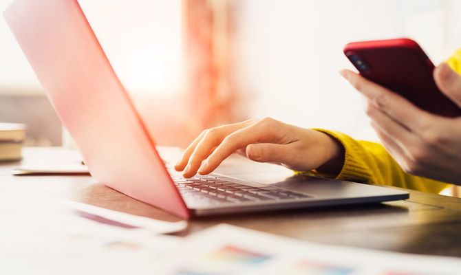 パソコンとスマートフォンを同時に操作する人の手