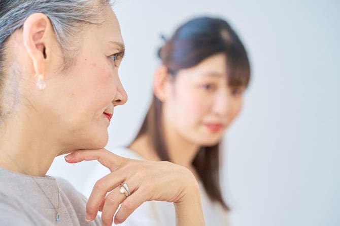 厳しい視線を投げるシニア女性を不安そうな若い女性が見つめている