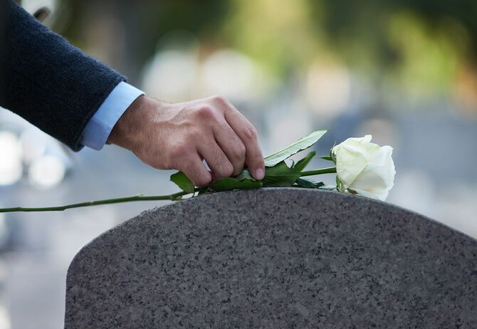 墓の上に白いバラを置く男性