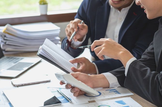 電卓とメモ帳を使用して打ち合わせをする2人のビジネスパーソン