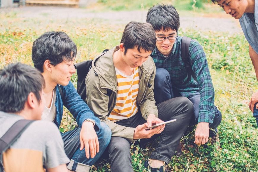 タブレット端末を見ながら話している男子大学生5人のグループ
