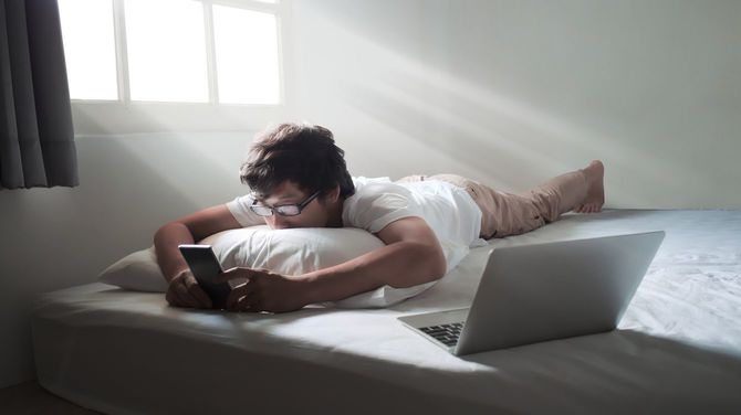 ベッドで横になってスマートフォンをいじる男性