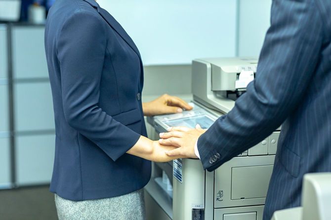 コピーを取っている女性に手を重ねる男性