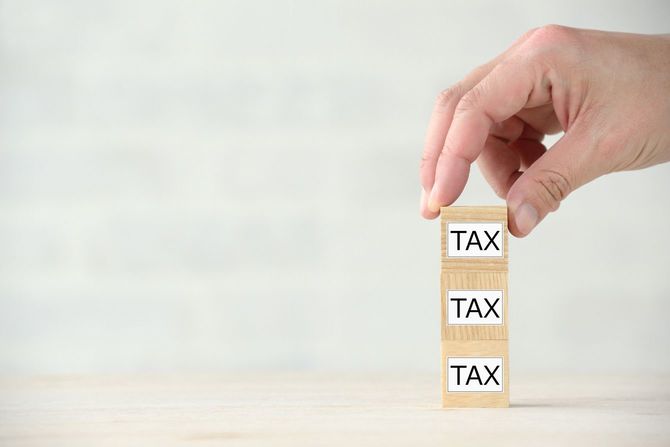 「TAX」と書かれた木製ブロックを上方に積み上げる手元