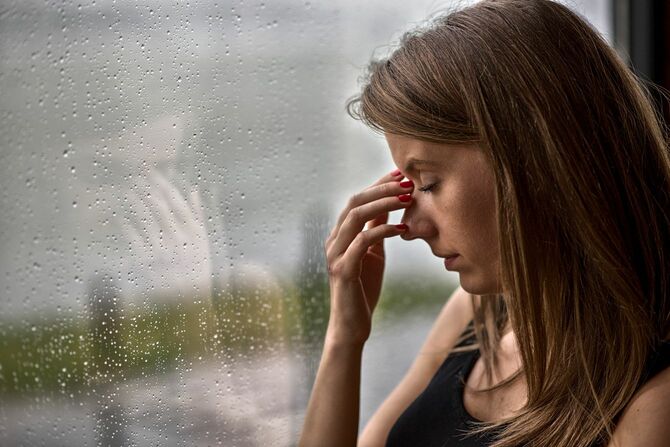 雨の日に窓のそばで頭痛をこらえている女性