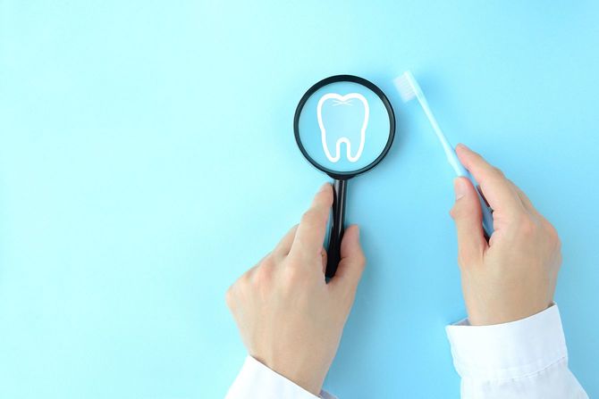 虫眼鏡と歯ブラシを持つ歯科医の手