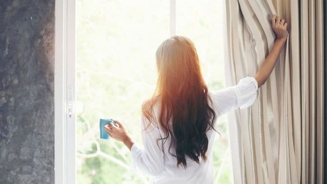 起床後、まずカーテンを開けて朝日を浴びる女性