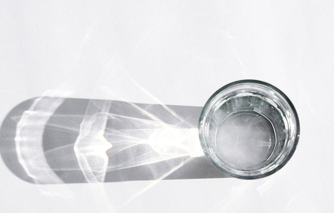 ガラスのコップに日光があたり、影と反射がテーブルに