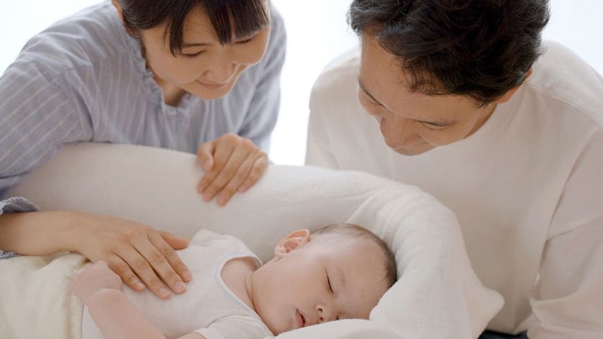 ベッドで眠る新生児を見守る両親