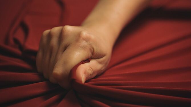 女性の手は情熱的に赤いベッドシーツを絞ります