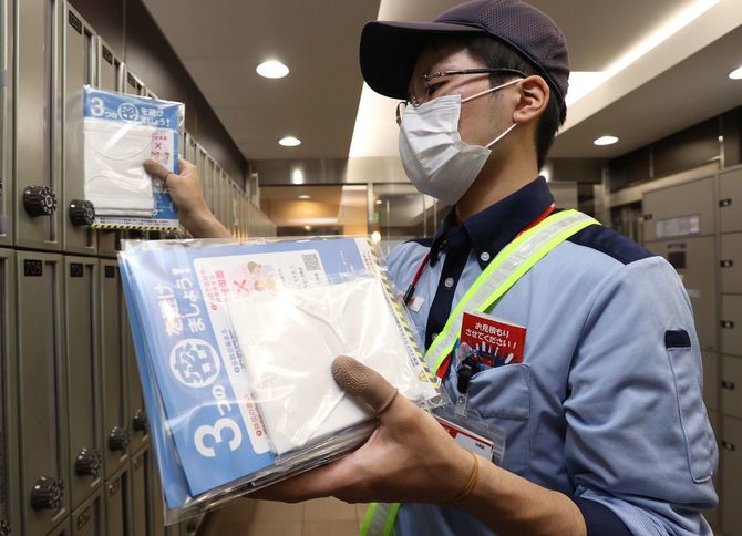 政府配布の布マスクをポストに投函する郵便局員＝2020年5月12日、大阪市内
