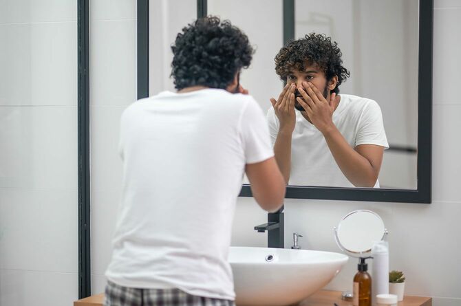 洗面所の鏡に映る自分の姿を見つめる男性