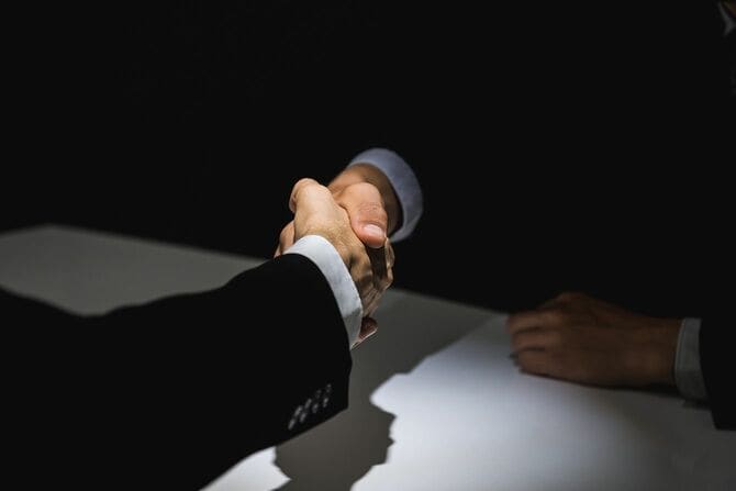 暗い影で握手をする匿名のビジネスパートナー