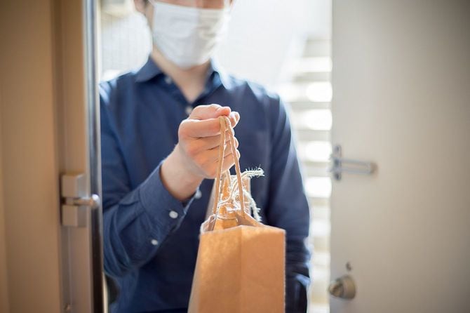 入り口で食べ物と紙袋を手渡すマスクを着用したアジア人男性