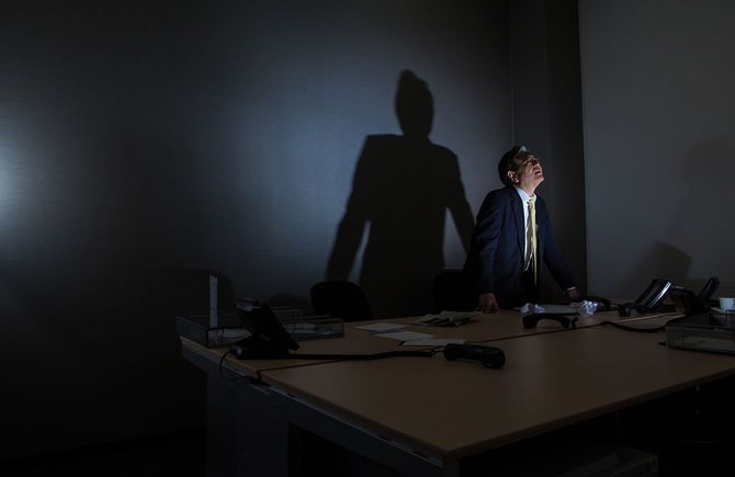 彼の会社が倒産している間、彼のオフィスで一人で座っている強調されたビジネスマン - 電話、書類、メモの混乱に囲まれて