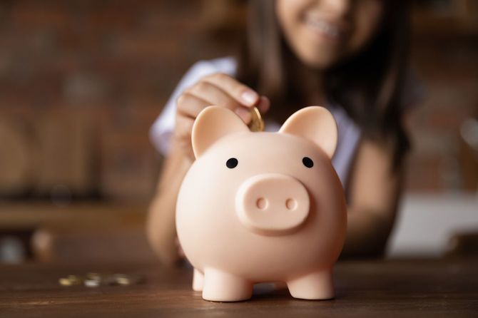 豚の貯金箱にコインを入れる少女