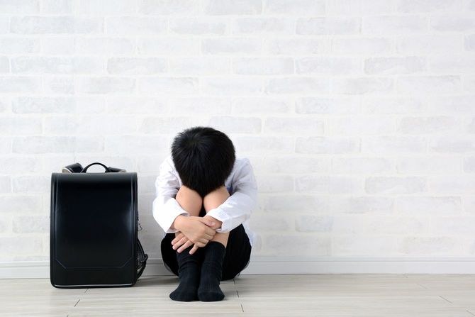 居間に一人で落ち込んだ様子で座っている子供と黒いランドセル