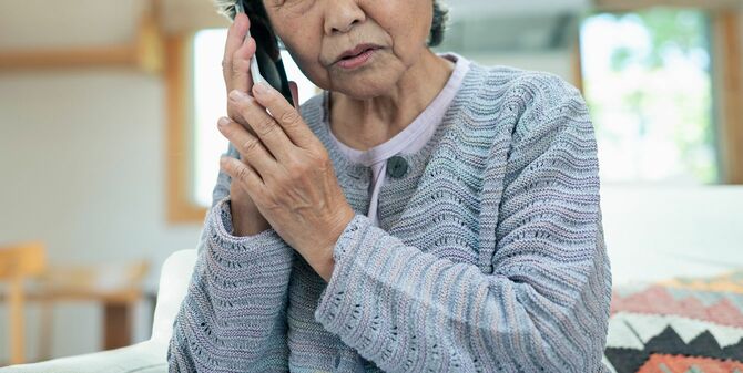 年配の女性が電話を受け、心配そうな表情